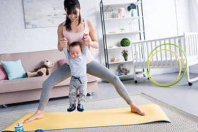 年轻的运动的母亲抱着小孩子, 而站在瑜伽垫在家