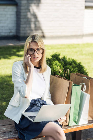 有吸引力的時(shí)尚女孩用智能手機(jī)交談, 坐在長凳上使用筆記本電腦袋