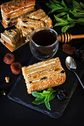 奶油和干果蛋糕。Medovik。蛋糕和一杯浓咖啡。蜂蜜蛋糕与干果 (干杏, 李子和坚果) 和浓咖啡在黑暗的背景。深色照片