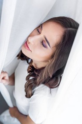 高角度观的美丽感性年轻女子闭上眼睛站在窗帘后面