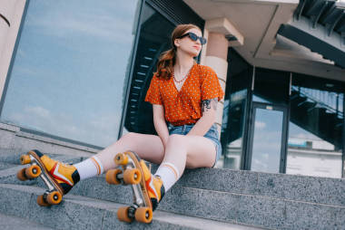 低角度的时尚女孩在轮滑鞋坐在楼梯上, 看着远离