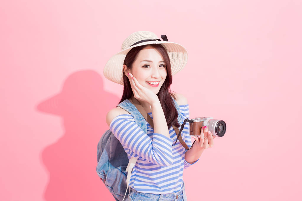 美丽的女人与相机愉快地微笑在粉红色的背景