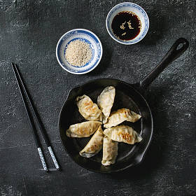 亚洲饺子 Gyozas 锅贴炒在铸铁锅上, 配有筷子和一碗酱油, 上面有黑色的纹理背景。顶部视图, 空间