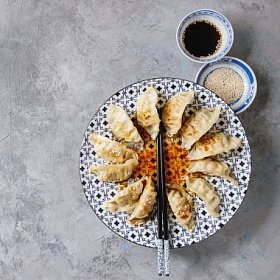亚洲饺子 Gyozas 锅贴在白色蓝色的陶瓷盘子上, 用筷子和一碗大豆芝麻酱在灰色纹理背景上供应。顶部视图, 复制空间