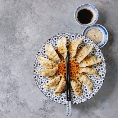 亚洲饺子 Gyozas 锅贴在白色蓝色的陶瓷盘子上, 用筷子和一碗大豆芝麻酱在灰色纹理背景上供应。顶部视图, 复制空间 亚洲饺子 Gyozas 锅贴在白色蓝色的陶瓷盘子上, 用筷子和一碗大豆芝麻酱在灰色纹理背景上供应。顶部视图, 复制空间