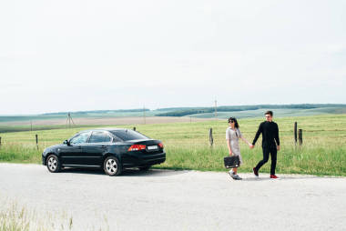 一對(duì)年輕的女孩和男孩舉行會(huì)談附近的黑色汽車(chē)背景藍(lán)天和田野