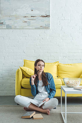 有吸引力的女孩拿着书, 看着相机, 而坐在地毯上, 在家学习