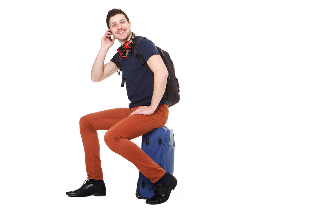 坐在手提箱上的男性旅行者肖像和手机通话 坐在手提箱上的男性旅行者肖像和手机通话