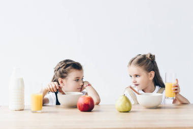 悲傷的女生吃谷類橙汁和水果, 看著彼此孤立的白色