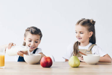 可愛的微笑的女學生倒入牛奶碗與谷物隔離白色