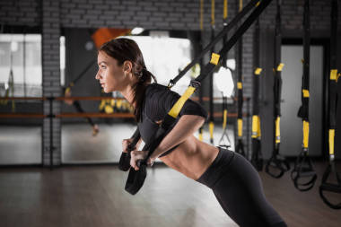 漂亮的健身女子訓(xùn)練與 trx 健身帶。體育館暫停運動