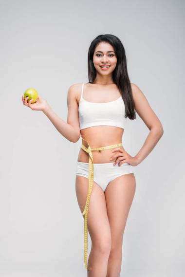 微笑苗條的非洲裔美國婦女與測量膠帶在腰圍持有蘋果, 孤立的灰色, 飲食概念