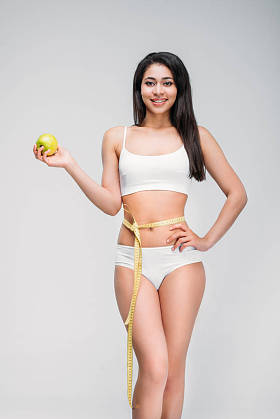 微笑苗条的非洲裔美国妇女与测量胶带在腰围持有苹果, 孤立的灰色, 饮食概念