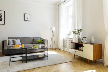 黑色桌子上的地毯前的灰色沙發(fā)在客廳內(nèi)部與櫥柜和海報。真實照片