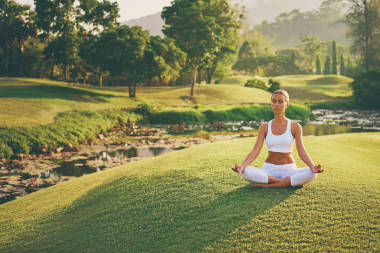 年轻妇女在莲花姿态坐在绿色草