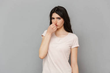 形象的不满年轻的女士站在灰色背景墙上看着相机覆盖他的鼻子