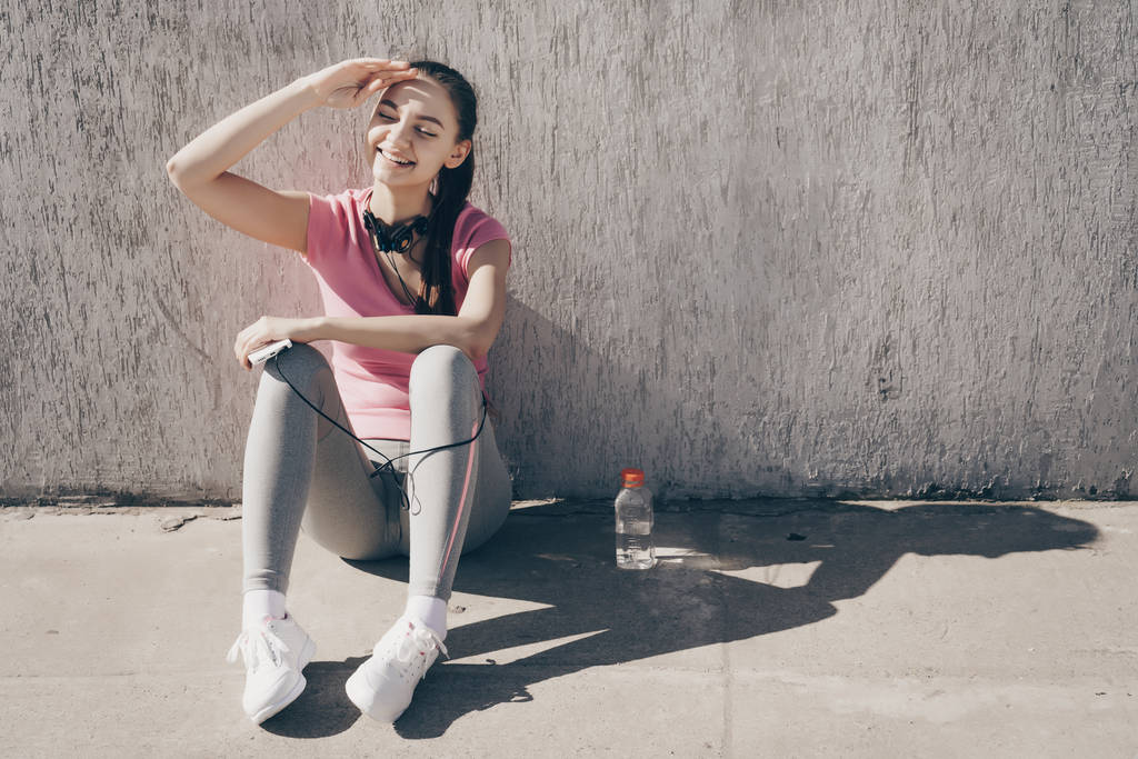 微笑的年轻女子坐在地上, 休息后, 一个艰苦的锻炼室外 微笑的年轻女子坐在地上, 休息后, 一个艰苦的锻炼室外