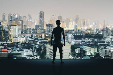 屋頂上的年輕人看著照亮的夜城的后面的看法。研究與成功理念 