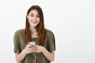 生活方式和美麗的人的概念。積極無憂無慮都市女性棕色頭發(fā), 聽好音樂在耳機, 微笑從滿意和幸福, 拿著智能手機在灰色墻壁上