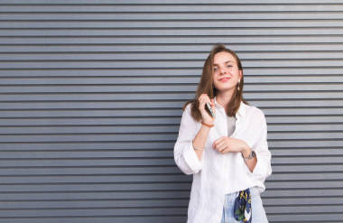 時尚迷人的女孩穿著淺色衣服看著相機和微笑, 站在灰色的背景上。一個美麗的女孩在黑暗條紋背景的肖像