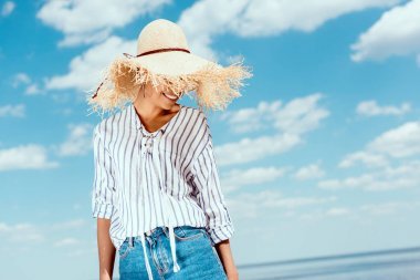 微笑非洲美国妇女在草帽反对蓝色多云天空