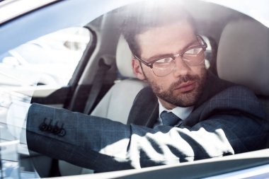 在駕駛汽車時(shí)看著眼鏡的商人的側(cè)面視圖