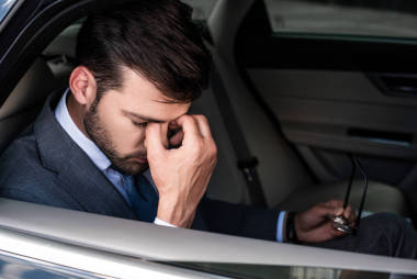坐在汽車后座上的戴眼鏡的疲憊商人的側面視圖