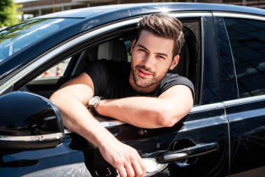 微笑英俊的年輕人坐在他的車肖像