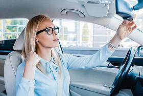 侧面视图的金发女商人在眼镜看后视镜在汽车