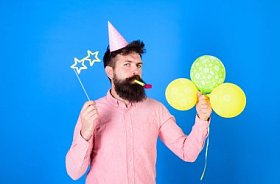 胡子党艺人在孩子庆祝, 国际儿童日概念。生日聚会上有明亮的气球、纸杯和帽子的男子。粉红色衬衫上的胡子时髦的蓝色背景