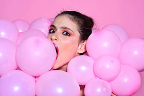 女孩梦想在强力粉彩趋势。复古的女孩与时尚的化妆和头发。生日装饰和庆祝。时尚女性与许多粉红色的气球。气球党在粉红色工作室背景
