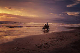日出时骑摩托车进入大海的人图片