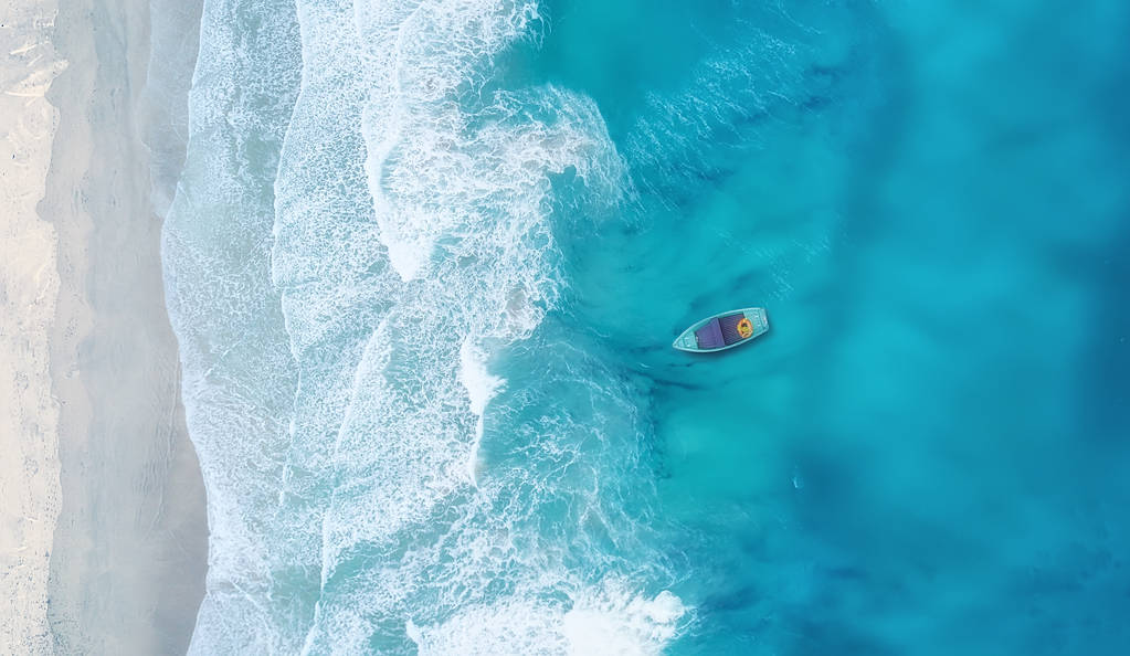 波浪和小船在海滩作为背景。美丽的自然背景在夏天时间从空气 波浪和小船在海滩作为背景。美丽的自然背景在夏天时间从空气