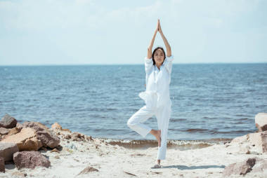亞洲女子站在海邊的 vrikshasana (樹姿) 上的前景色