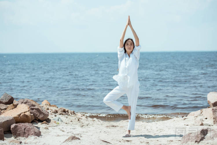 亞洲女子站在海邊的 vrikshasana (樹姿) 上的前景色
