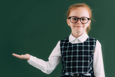可愛的小女生在眼鏡顯示空白黑板和微笑在照相機