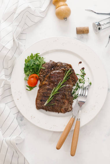 白色盤子上的芝麻菜和迷迭香樹枝牛排的頂部視圖