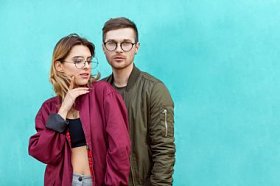 时尚情侣在他们的眼镜与勃艮第衣服摆在蓝色的木墙上