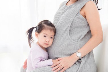 小亞洲女孩站在懷孕的母親和做嚴(yán)重的臉
