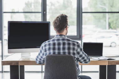 年轻程序员的后视图使用笔记本电脑和台式计算机