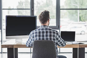 年轻程序员的后视图使用笔记本电脑和台式计算机