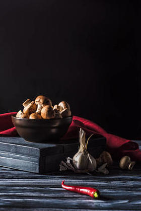 在黑色木桌上 champignons、大蒜和辣椒的碗的特写视图