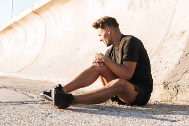 一名受傷的運(yùn)動(dòng)員在戶外坐著膝蓋疼痛的畫像