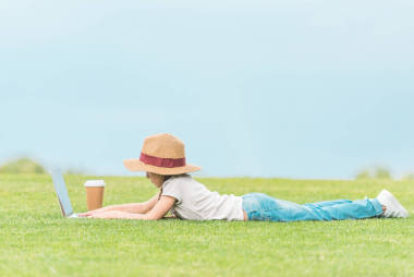 在綠色草地上使用膝上型電腦的可愛兒童的側(cè)面視圖