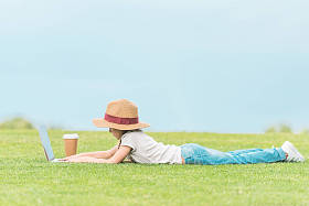 在绿色草地上使用膝上型电脑的可爱儿童的侧面视图