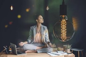 代表创造性思维的电灯泡和年轻的女实业家在工作台上的莲花位置沉思