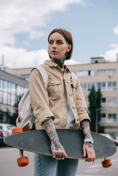 時尚紋身的女人看著遠(yuǎn)離和持有長板在街上