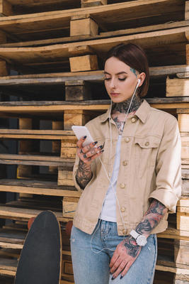 紋身時(shí)尚的女人在耳機(jī)聽音樂與智能手機(jī)在滑板附近