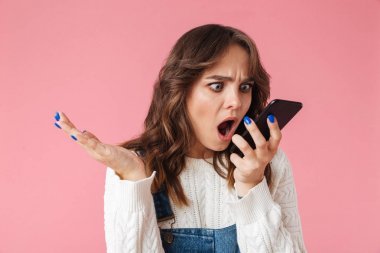 一個憤怒的年輕女孩的肖像在粉紅色背景下被隔離的手機大喊大叫