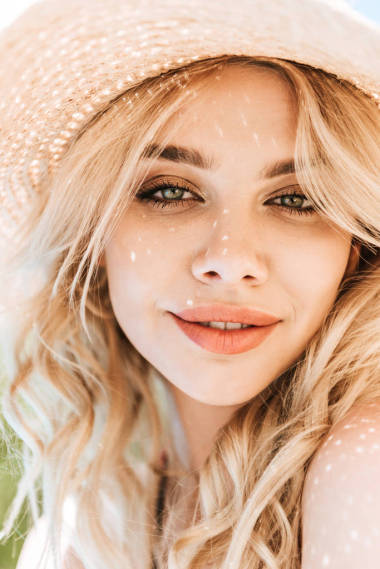 美麗的年輕金發(fā)女人的肖像在草帽微笑著在相機(jī)